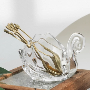 Elegant vintage swan glass jar with golden metal dessert spoons set on a wooden tray