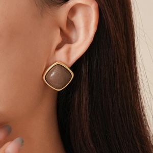 Close-up of vintage geometric square stud earrings with brown leather and gold frame on model