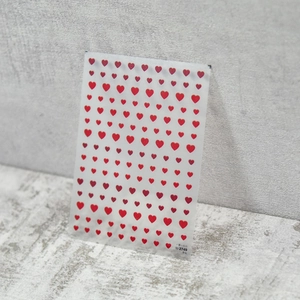 Detail view of thin red heart nail art stickers showing various sizes on transparent backing