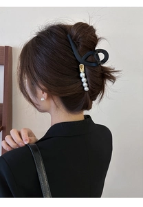 Détail de la pince à cheveux noire mate avec accents dorés et perles blanches sur modèle