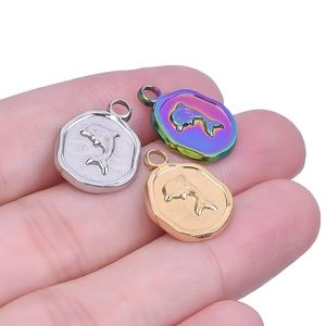 Hand holding three dolphin coin pendants in gold, silver, and rainbow stainless steel