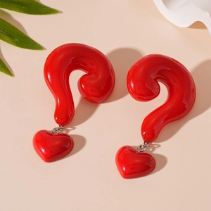Detailed view of red resin question mark and heart dangle earrings on a beige surface