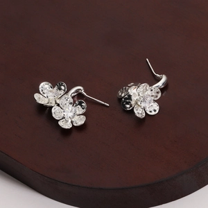 Close-up of silver flower stud earrings with zircon inlay on a dark wooden stand