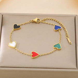 Macro detail of gold chain bracelet with colorful heart pendants on a jewelry cushion