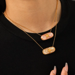 Close-up of model wearing gold necklaces with oval pink and beige shell stone pendants