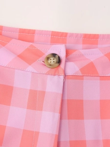 Detail of pink and orange plaid pattern with a faux tortoiseshell button on trousers