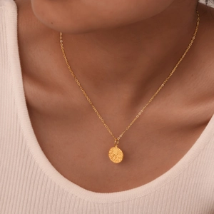Detailed view of a gold sunburst medallion pendant necklace worn on a female model