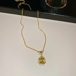 Macro shot of gold necklace featuring a green round gemstone surrounded by small diamonds