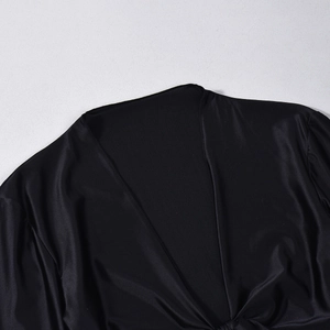 Detailed macro shot of silky black satin fabric with elegant deep V-neck and hem knot