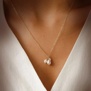Detailed view of baroque freshwater pearls on a gold chain worn with a white V-neck