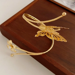 Detail of golden butterfly and daisy open cuff bracelet on dark wood base texture