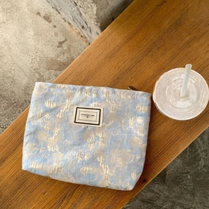 Macro view of blue jacquard makeup bag with silver floral pattern and woven label