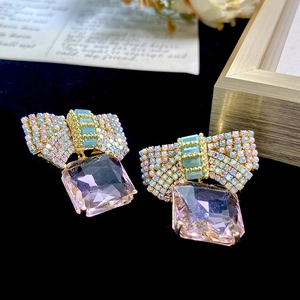 Detailed close-up of a pink bow earring with square crystal on a luxury black velvet background