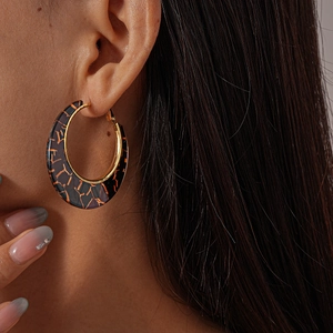 Close-up of a large black resin hoop earring with orange marble patterns and gold accents