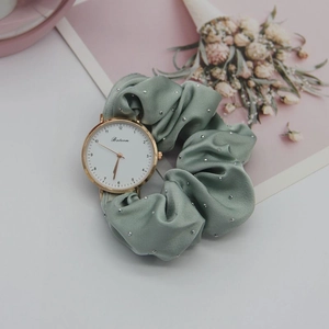 Elegant gold watch with light green ribbon strap and rhinestone details on white dial