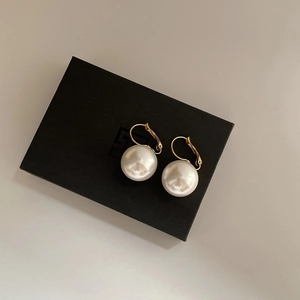 Detail of round white resin pearl drop earrings with 14K gold plating on black jewelry box