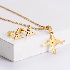 Minimalist gold heartbeat EKG jewelry set with necklace and earrings on white stone