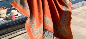 Vue détaillée du châle en tricot orange avec motifs de cœurs et pompons boho