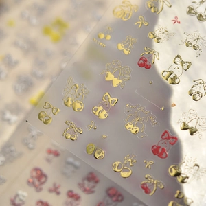 Macro detail of gold embossed cherry and bow nail art stickers with metallic texture