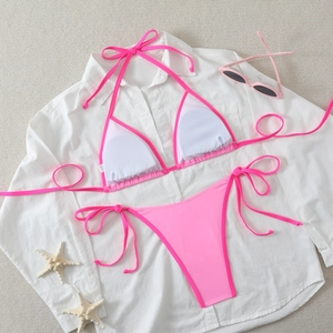 Neon pink criss-cross bikini set laid on white shirt with sunglasses and starfish props