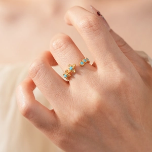 Gros plan d'une bague vintage dorée avec pierres turquoise et détails d'étoiles au doigt