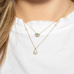 Detail of layered gold necklace with turquoise fan pendant and large pearl drop on model