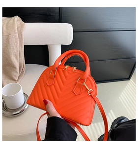 Detail view of orange shell bag with V-quilted faux leather and golden hardware