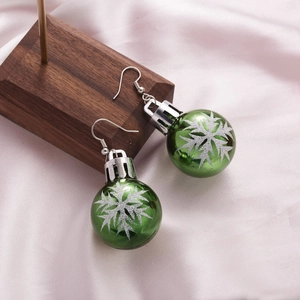 Detailed view of green Christmas ball earrings with silver snowflakes on silk background