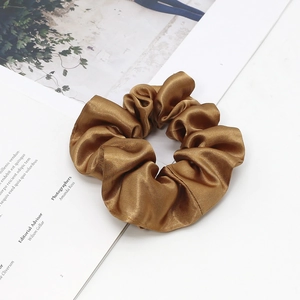 Close-up of golden satin scrunchie resting on a minimalist magazine with silk texture detail