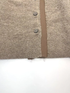 Close-up of oatmeal knit cardigan featuring frayed edges and dark round buttons
