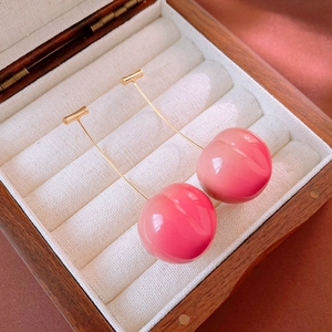 Cute pink resin peach long earrings with gold hooks on a white velvet jewelry box