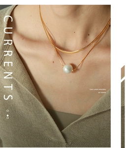 Detail of a double-layered gold blade chain necklace featuring a white cotton pearl pendant