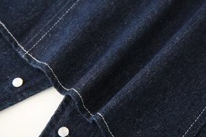 Close-up of dark blue denim fabric with silver metal buttons and white contrast stitching