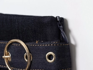 Détail du tissu denim bleu foncé avec coutures dorées et boucles métalliques