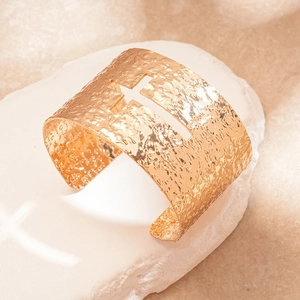 Macro detail of golden cross cutout cuff bracelet with textured hammer finish surface