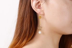 Détail d'une boucle d'oreille étoile dorée avec perle et tige longue portée par modèle