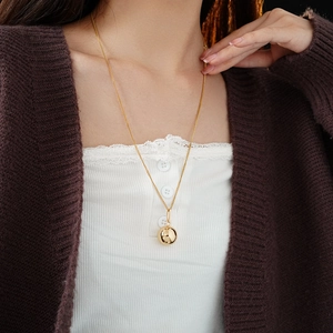 Detail of a metallic gold sphere pendant necklace on a model showing minimalist style