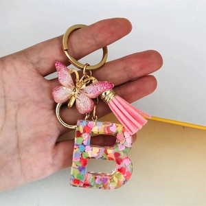 Detail of pink resin letter B keychain with butterfly charm and glitter sequins