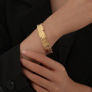 Elegant gold feather-shaped open cuff bracelet in titanium steel on a model's wrist