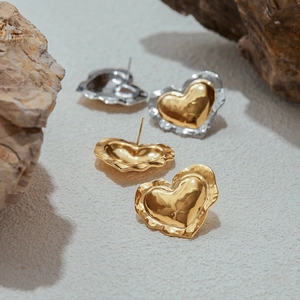 Macro shot of irregular heart earrings in gold and silver on natural stone background