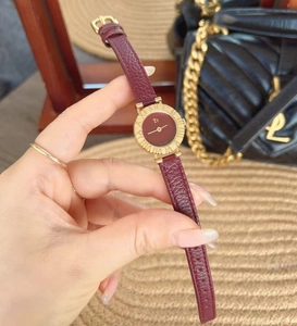 Detail of red leather strap watch with gold case held against a designer bag