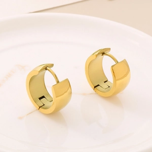 Detailed close-up of wide polished 18K gold-plated huggie earrings on a porcelain plate