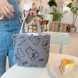 Close-up of a grey corduroy tote bag featuring a cute bear pattern in a cafe setting