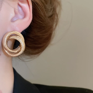 Close-up of matte gold interwoven triple hoop earrings worn for a stylish look