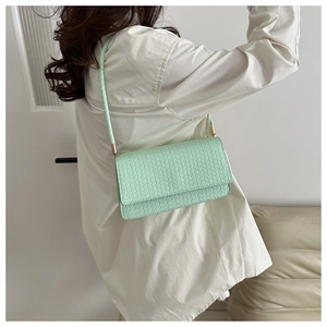 Close-up of mint green woven shoulder bag with gold metal hardware and flap closure