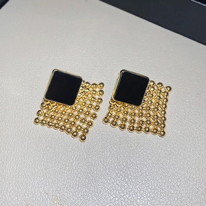Macro detail of geometric woven diamond earrings featuring gold metal and black enamel