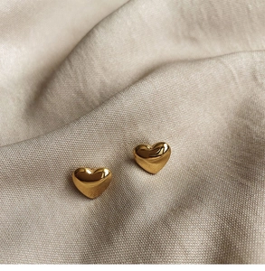 Macro shot of polished 18K gold titanium heart stud earrings on champagne silk fabric