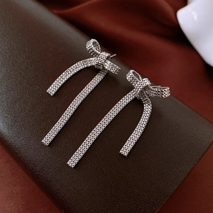 Macro detail of silver bow earrings with woven mesh texture and long flowing tassels