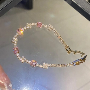 Elegant gold tennis bracelet with pink square zircons and white crystals on a glass surface