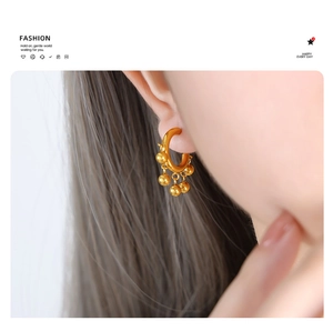 Close-up of a gold C-shaped earring with dangling beads worn by a fashion model